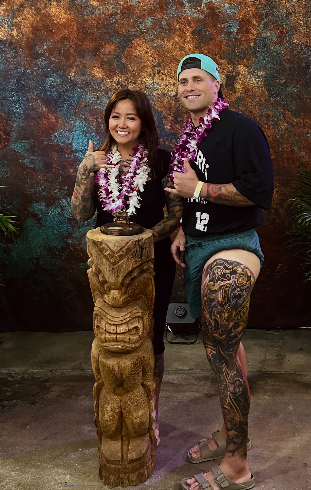 Lynn Hoang and a client beside a carved tiki with an award-winning leg sleeve